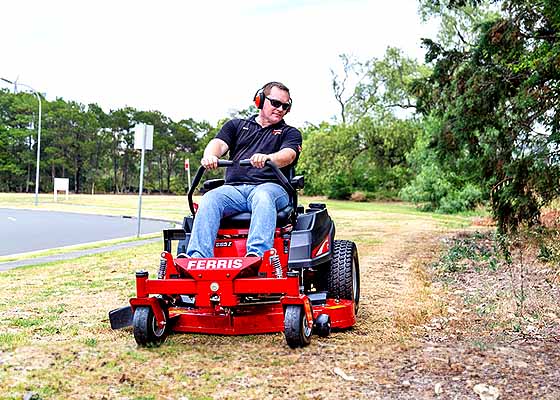 Man with headphones riding a ferris mower.